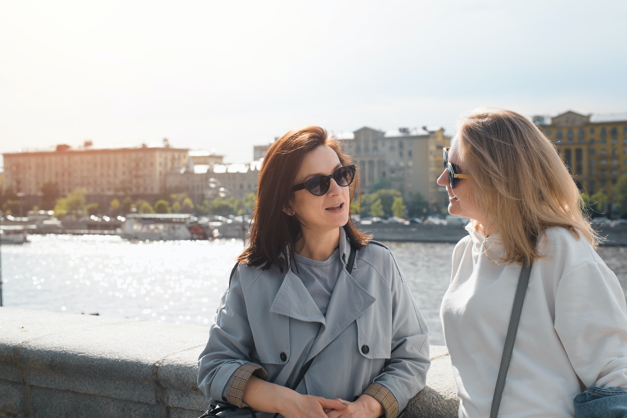 Two young women talking outdoors. Joyful friends standing against the backdrop of the city and