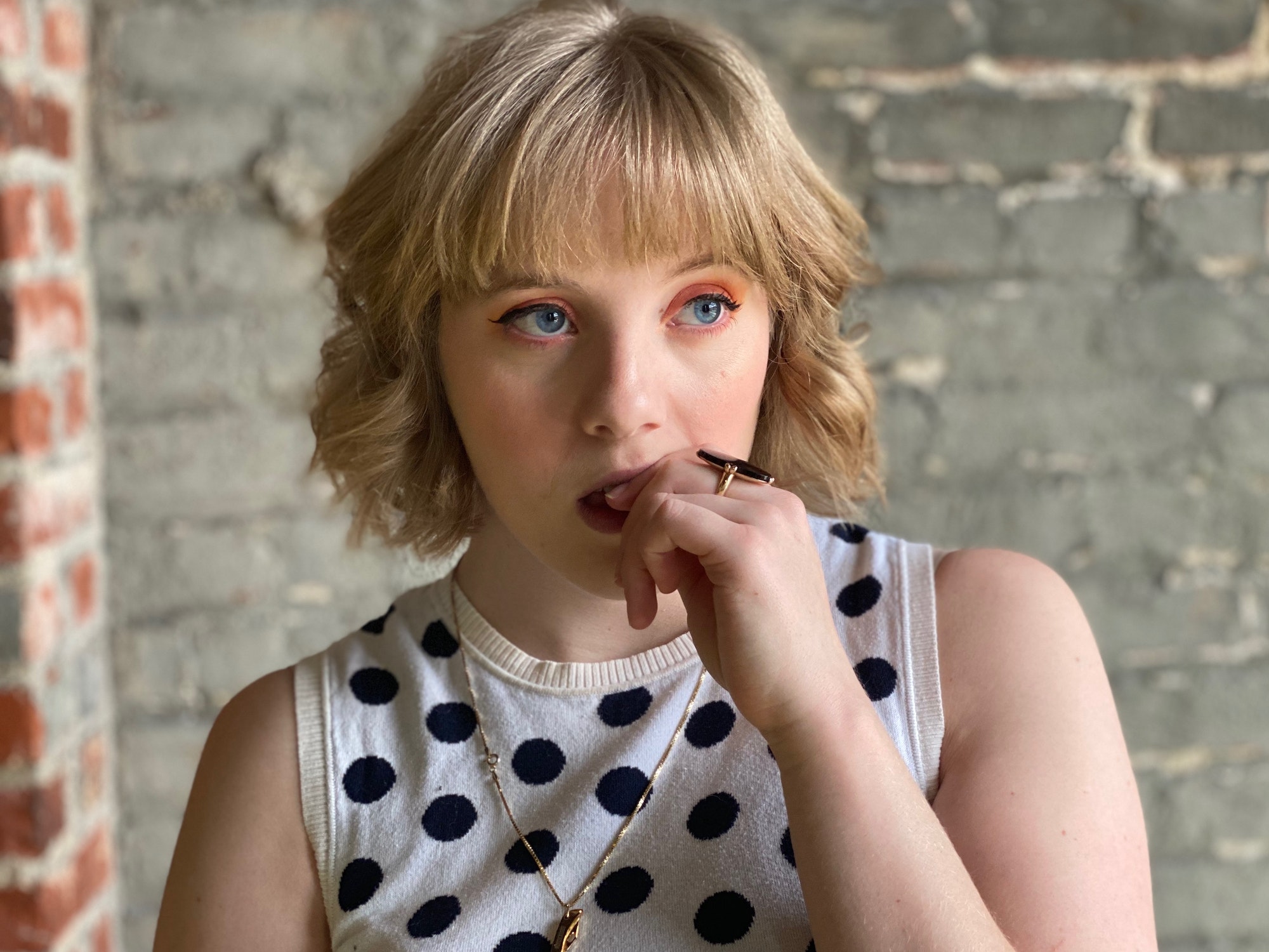 A millennial woman in polka dots bites her nails and looks worried or anxious